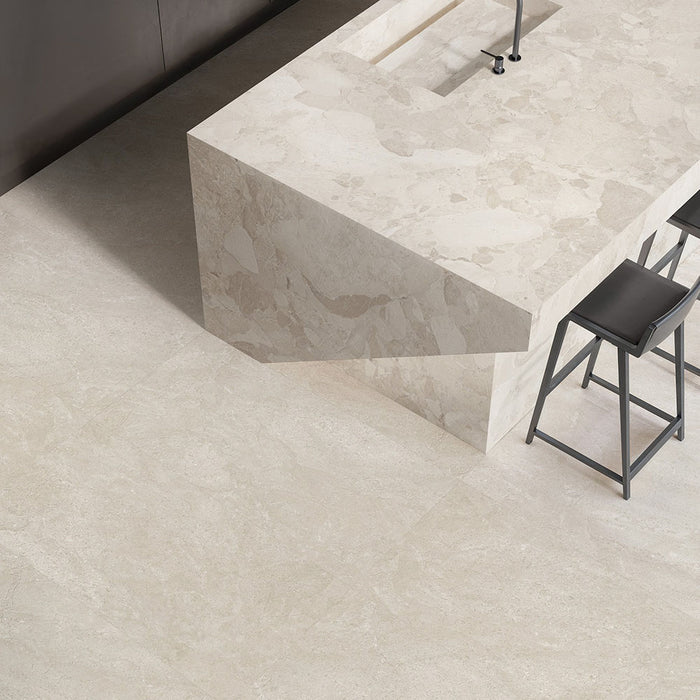 Contemporary kitchen featuring Jeddah Avorio Neutra Stone 30x60cm stone-effect wall and floor tiles, showcasing warm ivory and beige tones, paired with a matching waterfall island, black bar stools and minimalist finishes.