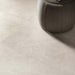 Close-up of Jeddah Avorio Neutra Stone 30x60cm stone-effect floor tiles, showcasing warm ivory and beige tones with delicate natural stone-inspired veining, paired with a soft upholstered pouffe in a contemporary interior.