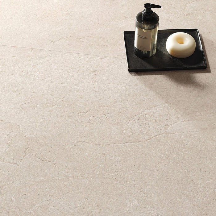 Close-up of Jeddah Avorio Neutra Stone 60x60cm stone-effect floor tiles, showcasing warm ivory and beige tones with delicate natural stone-inspired veining, styled with a black tray, soap dispenser and minimalist bathroom accessories.