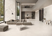 Contemporary living space featuring Jeddah Blanco Neutra Stone 30x60cm stone-effect wall and floor tiles, showcasing soft cream and ivory tones, paired with minimalist furniture, floor-to-ceiling glazing and warm natural textures.