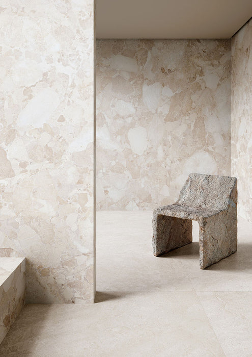 Interior featuring Jeddah Blanco Neutra Stone 30x60cm stone-effect wall and floor tiles, showcasing soft cream and ivory tones with natural stone-inspired detailing, paired with a sculptural stone chair in a minimalist contemporary space.