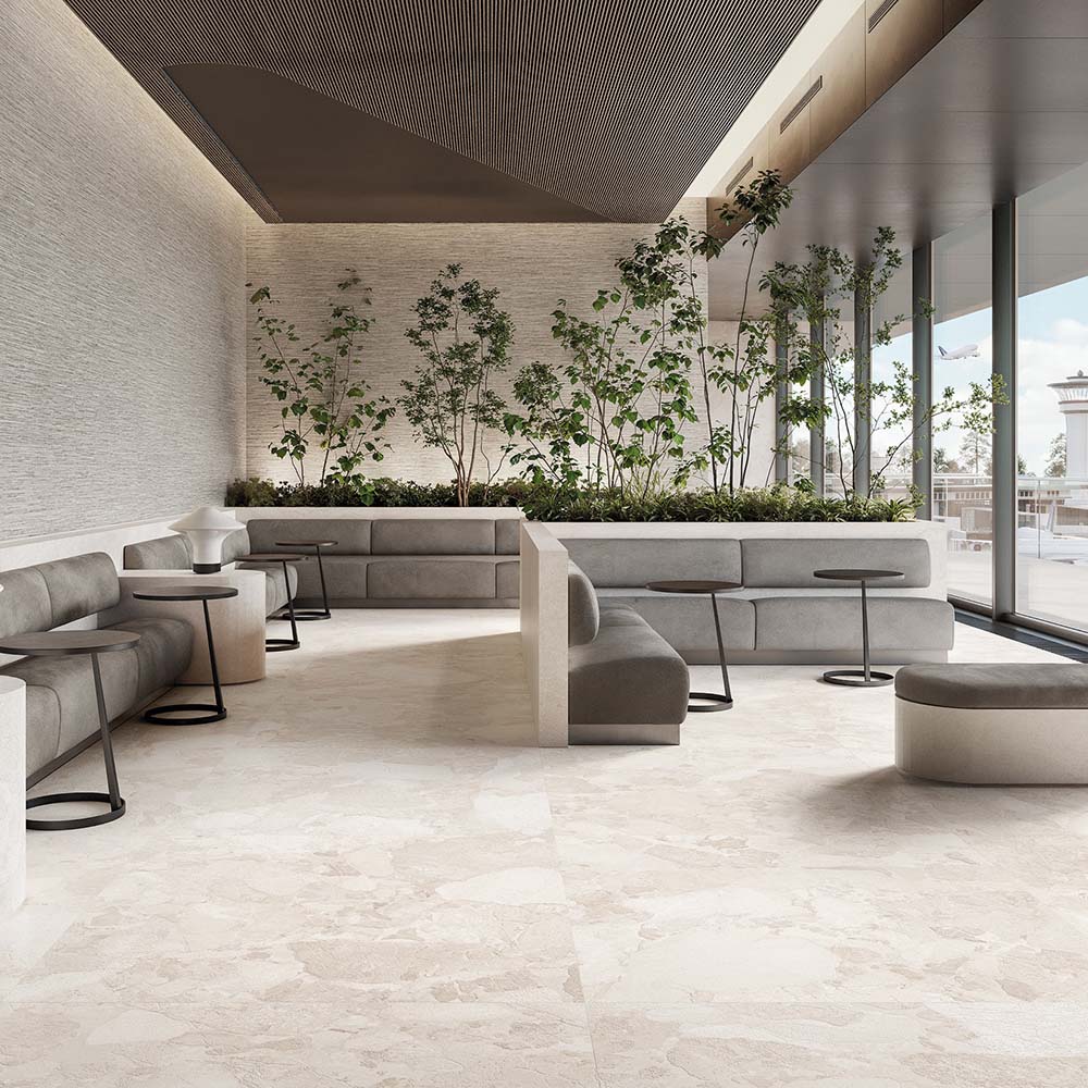 Contemporary lounge featuring Jeddah Blanco Sassi Terrazzo Stone 60x120cm stone-effect floor tiles, showcasing soft cream and beige tones with natural stone-inspired detailing, paired with minimalist seating, indoor planting and floor-to-ceiling glazing.