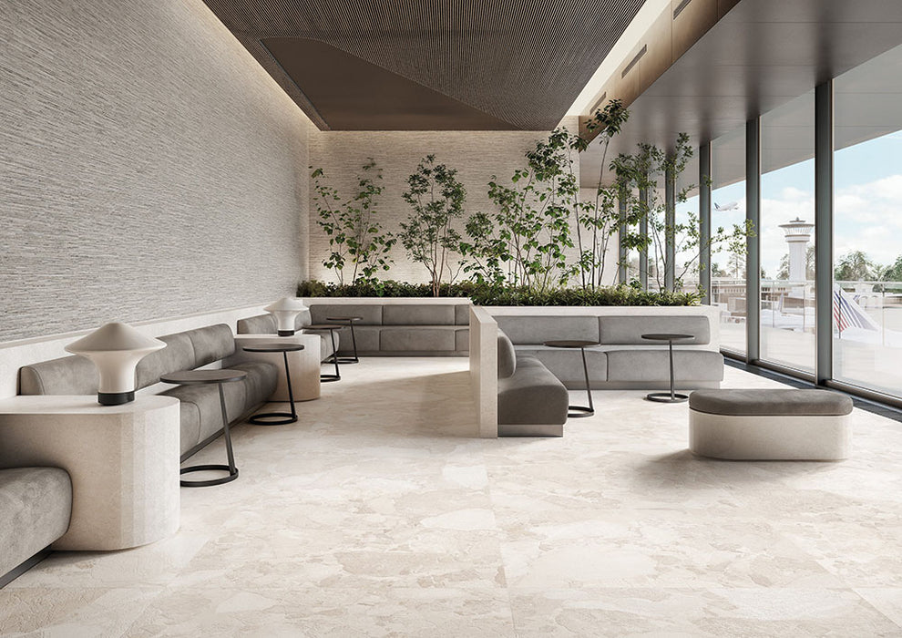 Contemporary lounge featuring Jeddah Blanco Sassi Terrazzo Stone 60x120cm stone-effect floor tiles, showcasing soft cream and beige tones with natural stone-inspired detailing, paired with minimalist seating, indoor planting and floor-to-ceiling glazing.