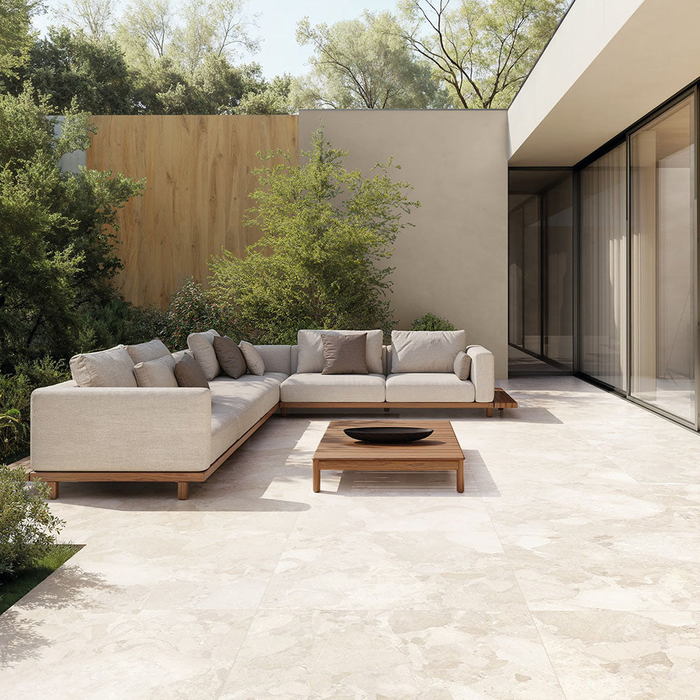 Contemporary outdoor patio featuring Riad Blanco Terrazzo 20mm 100x100cm outdoor stone-effect porcelain tile slabs, showcasing soft cream and beige tones, paired with minimalist lounge seating, timber furniture and landscaped gardens.