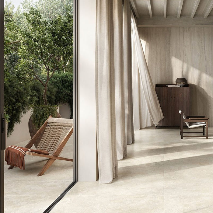 Living room featuring Jesi Travertine 60x60cm wall and floor tiles, showcasing soft travertine effect surfaces in warm cream and beige tones, paired with natural wood furniture, flowing linen curtains and minimalist styling for a calm, contemporary interior.