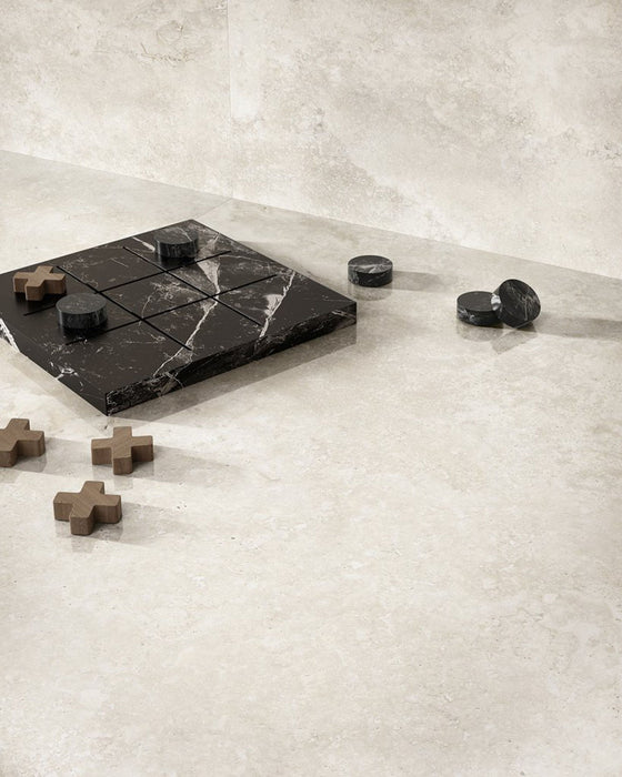Lifestyle image featuring Jesi Travertine 60x60cm wall and floor tiles, showcasing soft travertine effect detailing in warm cream and beige tones, paired with a black marble chess set and natural wood accessories for a calm, contemporary interior.
