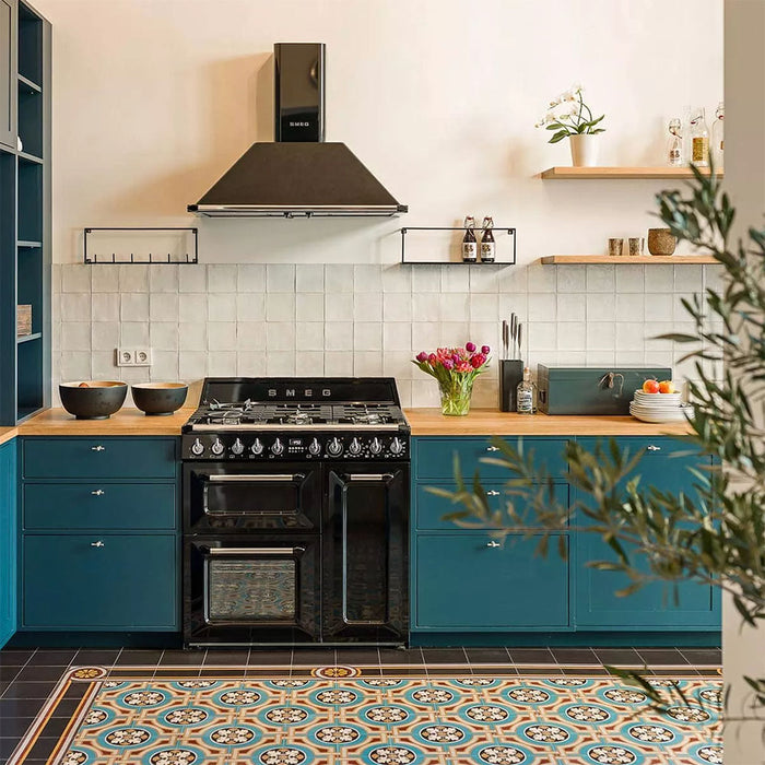 Kitchen interior featuring Europa Helsinki 20x20cm Victorian Moroccan style floor tiles in teal, terracotta and cream tones, installed with a decorative border and styled with teal cabinets, wooden worktops and a black range cooker.