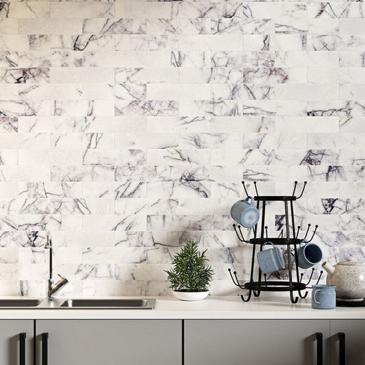 Kitchen interior featuring Fitzrovia Lilac 5 x 20cm honed natural marble tiles installed in a staggered brick layout, showcasing a soft white base with delicate lilac-grey veining, styled with a clean worktop, black accents, and subtle greenery for a contemporary, design-led finish.