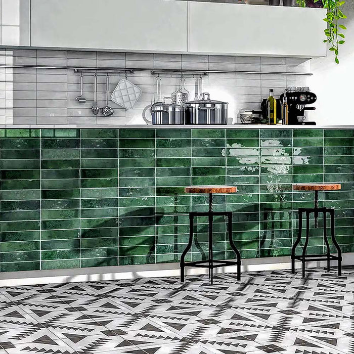Contemporary kitchen featuring Izmir Brick Green Gloss 6x25cm ceramic wall tiles, styled with monochrome geometric floor tiles, white cabinets, and industrial bar stools for a bold modern look.