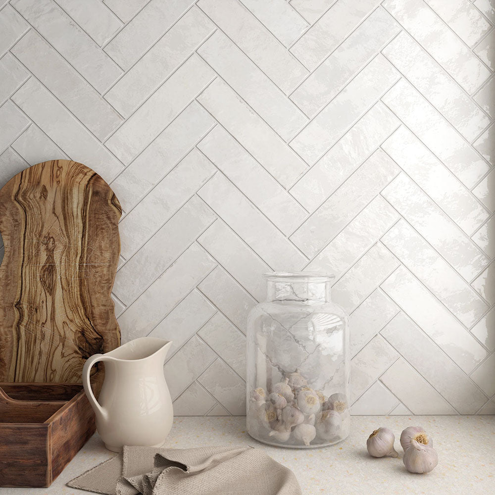 Madison White Brick Wall Tiles 6x24.6cm — shown in a stylish kitchen setting with a classic herringbone layout, natural wood accents, and soft lighting. These glossy white tiles bring a bright, handcrafted finish that elevates modern and rustic spaces alike.