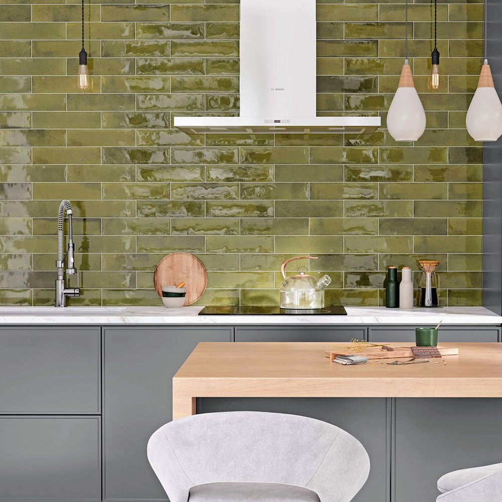 Modern kitchen featuring Izmir Brick Daisy Green Gloss 6x25cm ceramic wall tiles, styled with grey cabinetry, white marble-effect countertops, wooden accents, and contemporary pendant lighting.