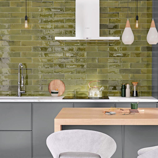 Modern kitchen featuring Izmir Brick Daisy Green Gloss 6x25cm ceramic wall tiles, styled with grey cabinetry, white marble-effect countertops, wooden accents, and contemporary pendant lighting.