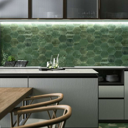 Contemporary kitchen featuring Izmir Hexagon Green Gloss 15x17.3cm ceramic wall tiles, styled with light grey cabinetry, wooden bar stools, marble countertops, and under-cabinet lighting for a sleek modern look.