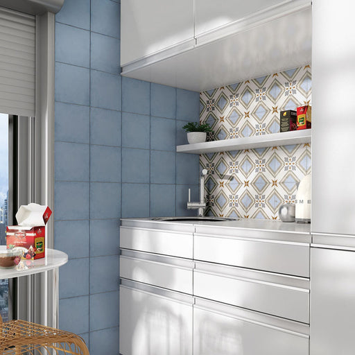 Kitchen setting featuring Carnaby Turner Victorian-style 20x20cm porcelain wall and floor tiles used as a patterned backsplash, displaying a blue, gold, and cream geometric design, paired with soft blue wall tiles, white cabinetry, and modern shelving.