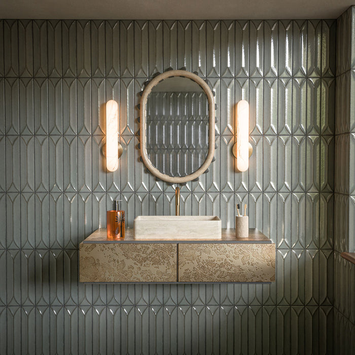 Contemporary bathroom featuring Kutani Decor Lichen Green porcelain wall tiles in a 9.1cm x 37.5cm format, creating a geometric feature wall behind a floating vanity with brass accents and soft ambient lighting.