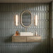 Contemporary bathroom featuring Kutani Decor Lichen Green porcelain wall tiles in a 9.1cm x 37.5cm format, creating a geometric feature wall behind a floating vanity with brass accents and soft ambient lighting.