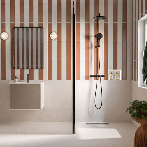 Kutani Vanilla 9.1cm x 37.5cm porcelain wall tiles, arranged vertically across a contemporary bathroom in warm cream tones, paired with contrasting terracotta tiles, terrazzo effect flooring and black fittings.