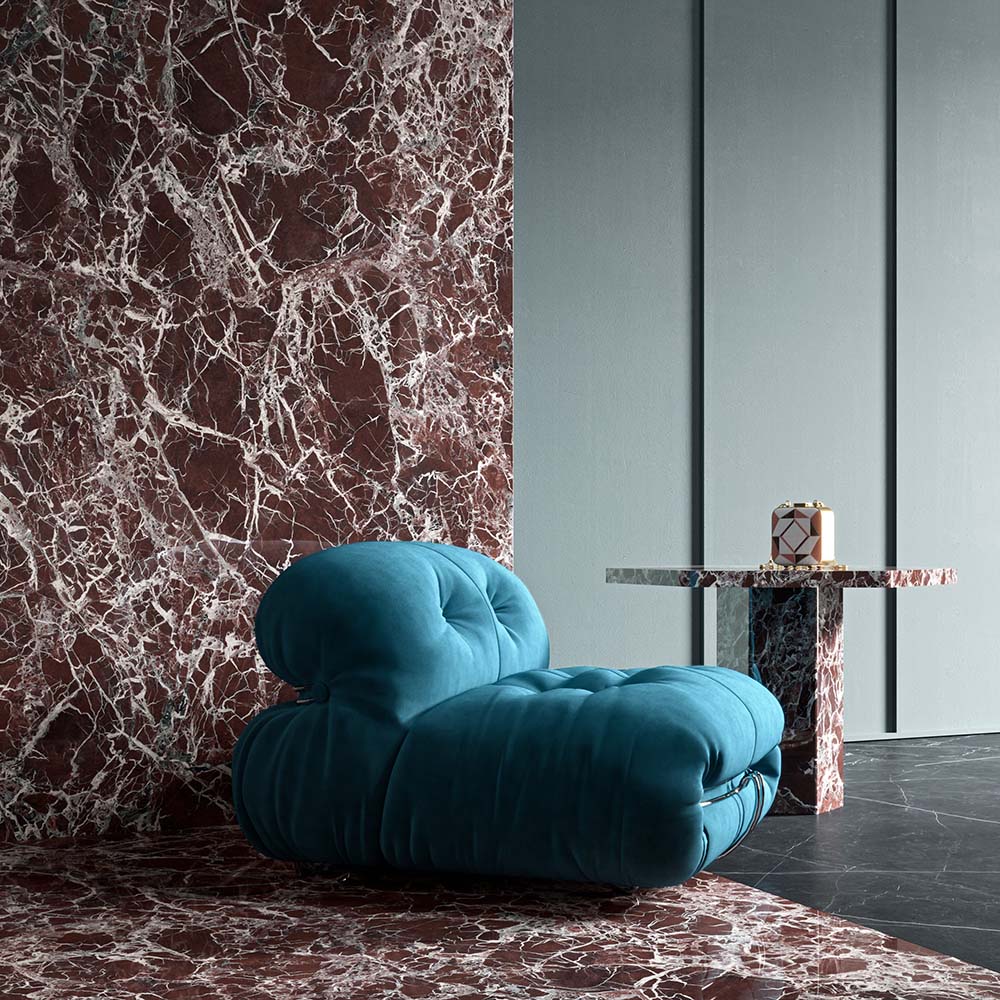 Living space featuring Grand Levant Rouge Polished Marble effect 60 × 120cm porcelain wall and floor tiles, styled with a sculptural blue armchair, marble side table, and bold red tones with striking white veining.