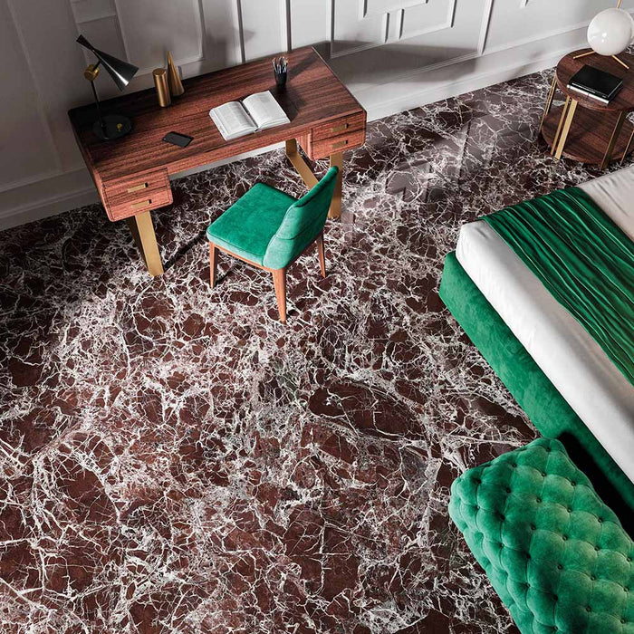 Bedroom interior featuring Grand Levant Rouge Polished Marble effect 60 × 120cm porcelain floor tiles, styled with rich wood furniture, green velvet seating, and dramatic red tones with striking white veining.
