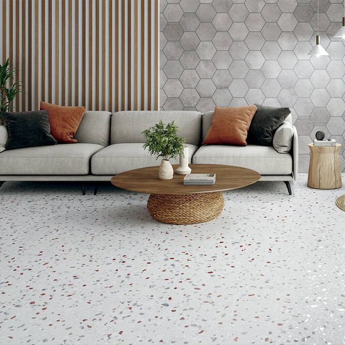 Living room featuring Confetti Colours 66×66cm terrazzo-style porcelain floor tiles with multicoloured chips on a white base, styled with a neutral sofa, wooden slat wall, grey hexagon feature wall, and a round woven coffee table for a modern, warm aesthetic.