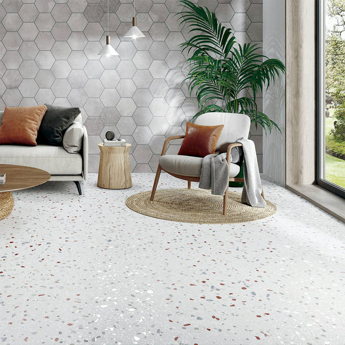 Living room featuring Confetti Colours 66×66cm terrazzo-style porcelain floor tiles with multicoloured chips on a white base, styled with a neutral sofa, wooden slat wall, grey hexagon feature wall, and a round woven coffee table for a modern, warm aesthetic.
