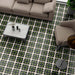 Living room featuring Geometry Illusion Verde Noir 20x20cm geometric patterned floor tiles in deep green, black, and cream tones, styled with neutral upholstered sofas, a marble-topped coffee table, and modern decor.