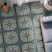 Living room interior featuring Europa Gothenberg 20x20cm Victorian Moroccan style floor tiles in blue, mint green and cream tones, styled with a grey sofa, floor lamp, curtains and decorative vase in a bright interior setting.