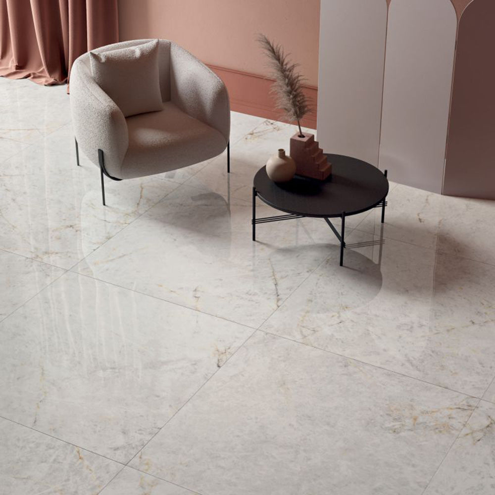 Living area featuring Grand Mahal Matt Marble effect 60 × 60cm porcelain floor tiles, showcasing a soft ivory base with delicate gold and beige veining, paired with neutral furnishings, a black coffee table, and warm blush tones for a calm, contemporary finish.