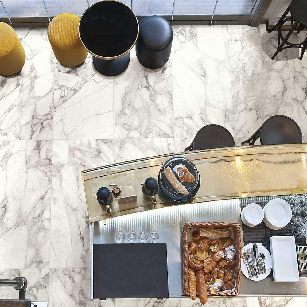 Top-down view of Maine Calacatta Matt Marble 30 × 60cm porcelain floor tiles, showcasing a soft white base with elegant grey veining, styled within a café setting with warm metallic accents and contemporary furnishings for a refined, modern look.
