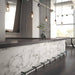 Bar and dining setting featuring Maine Calacatta Matt Marble 60 × 60cm porcelain wall tiles, styled across the counter front to showcase soft grey veining on a clean white base, paired with dark worktops, industrial lighting, and polished concrete for a refined, contemporary contrast.