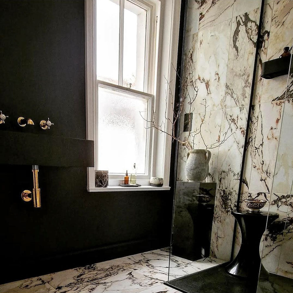 Bathroom interior featuring Maine Capraia Matt Marble 60 × 60cm porcelain wall and floor tiles, styled with bold dark veining against a soft white base, paired with black fixtures and warm brass accents for a striking, contemporary contrast.
