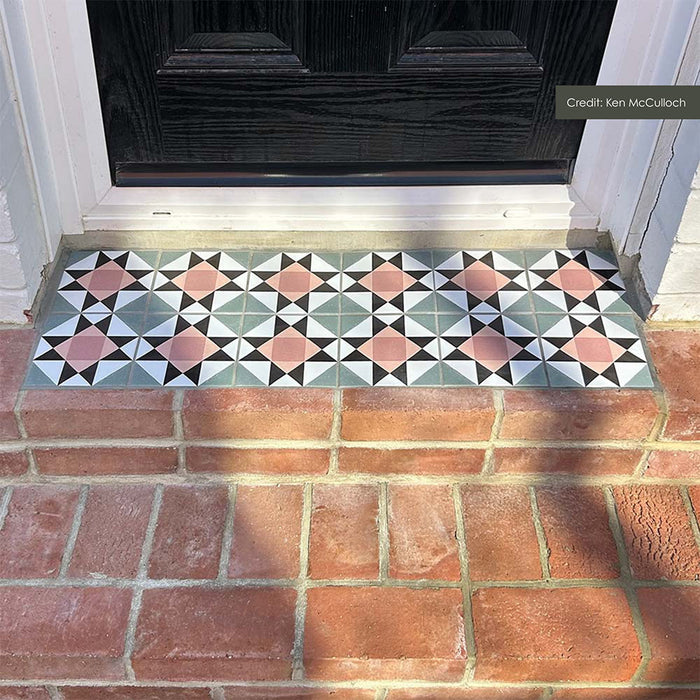 Outdoor doorstep featuring Maison MINI Fern 15cm x 15cm Victorian style tiles, showcasing a geometric star pattern in soft green, pink, black and white, paired with traditional red brickwork and a black front door.