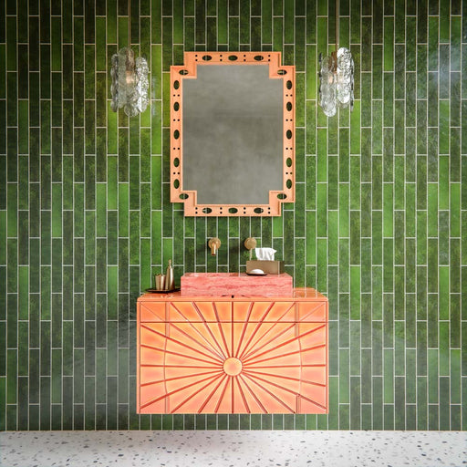 Bathroom feature wall showcasing Malaga Tourmaline Green Brick 6.5 × 32.8cm gloss ceramic wall tiles, laid in a vertical stacked pattern with deep green tonal variation and a glossy handcrafted finish, paired with a statement coral vanity unit, brushed brass fittings, and decorative lighting for a bold, design-led interior.
