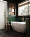 Bathroom interior featuring Maldives Pine Green 5 × 40cm gloss ceramic wall tiles, laid horizontally with rich green tonal variation, paired with a freestanding bath, brass fittings, wood shelving, and dark marble-effect flooring.