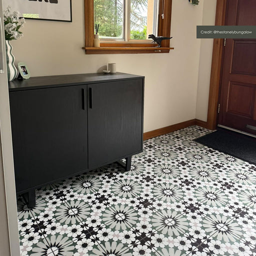 Hallway interior featuring Fizaan Orchid Green 20x20cm Moroccan-style porcelain floor tiles, showcasing a repeating geometric pattern in green, black and soft neutral tones, styled with a modern black sideboard.