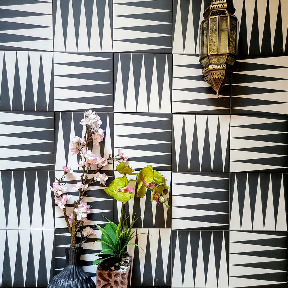 Alhambra Tavla 20x20cm Moroccan tiles arranged on a feature wall, showcasing a bold black and white triangular geometric pattern with decorative lantern and floral accents for an authentic Moroccan look.