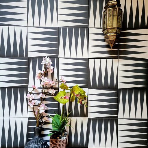 Alhambra Tavla 20x20cm Moroccan tiles arranged on a feature wall, showcasing a bold black and white triangular geometric pattern with decorative lantern and floral accents for an authentic Moroccan look.