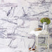 Interior setting featuring Fitzrovia Lilac 30.5 x 61cm honed natural marble tiles installed in a staggered brick layout, showcasing soft white tones with flowing lilac-grey veining, styled with a rustic stool, soft textiles, and decorative accents for a calm, considered finish.