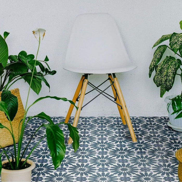 Interior setting featuring Fizaan Federal Blue 20x20cm Moroccan-style porcelain floor tiles, showcasing a repeating geometric pattern in deep blue and soft neutral tones, styled with a modern white chair and greenery.