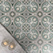 Overhead view of Europa Toulouse 20x20cm Victorian Moroccan style floor tiles in green, grey and cream tones, forming a decorative repeating pattern, styled with a soft grey rug and candles in a cosy interior setting.