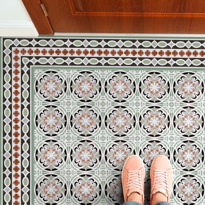 Empire Green Corner 15x15cm Victorian floor tiles with matching border, featuring an ornate floral and geometric pattern in sage green, terracotta, and white tones, styled in a hallway setting with wooden door and pink shoes for scale.
