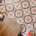 Overhead view of Europa Dortmund 20x20cm Victorian Moroccan style floor tiles in red, cream, grey and black tones, forming a decorative repeating pattern, styled with wooden furniture and magazines in an interior setting.