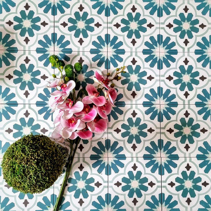 Flatlay featuring Clarence House Teal Green 20x20cm Victorian Moroccan-style porcelain tiles, styled with pink orchids and green foliage to highlight the bold teal and white geometric pattern.
