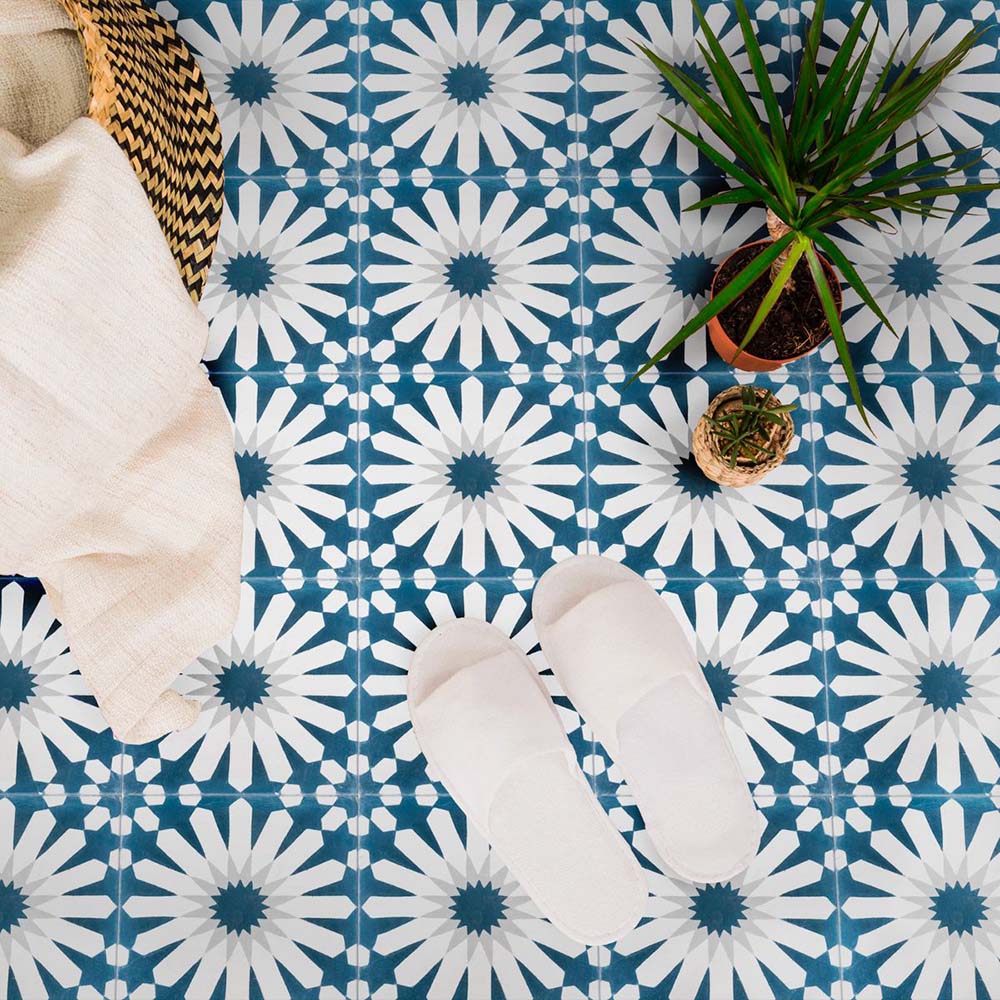 Marketing setting featuring Soukaina Blue B Moroccan-style 20cm x 20cm patterned porcelain floor tiles, showcasing a bold geometric star design in rich blue and white tones with a matt finish, styled with soft textiles and greenery.