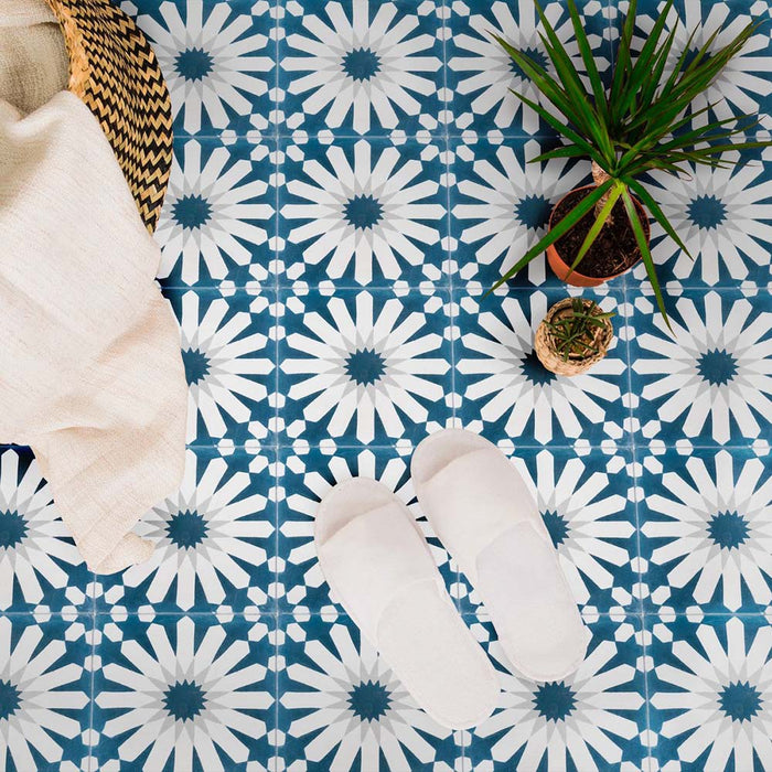 Marketing setting featuring Soukaina Blue B Moroccan-style 20cm x 20cm patterned porcelain floor tiles, showcasing a bold geometric star design in rich blue and white tones with a matt finish, styled with soft textiles and greenery.