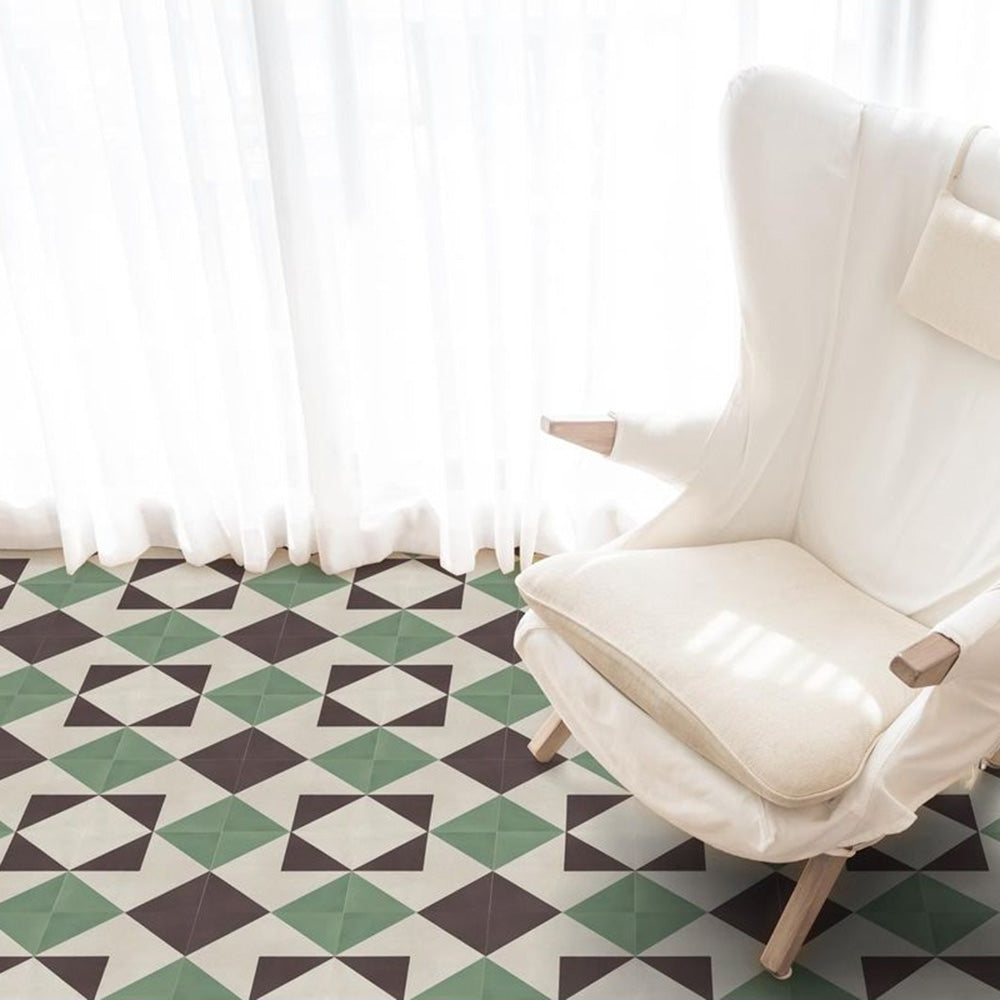 Living room setting featuring Geometry Angles Patterned Tile in 20cm x 20cm, arranged in a repeating geometric pattern with green, black, and off-white triangular shapes. A soft white armchair sits on the tiled floor beside sheer white curtains, creating a bright and airy atmosphere.