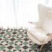 Living room setting featuring Geometry Angles Patterned Tile in 20cm x 20cm, arranged in a repeating geometric pattern with green, black, and off-white triangular shapes. A soft white armchair sits on the tiled floor beside sheer white curtains, creating a bright and airy atmosphere.