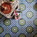 Decorative interior featuring Fizaan Springs Moroccan-style 20×20cm porcelain floor tiles, showcasing a blue and green geometric pattern styled with bohemian décor and indoor plants.
