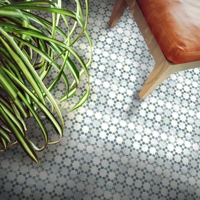Bedouin Mequinez Green Moroccan-style 15x15cm patterned floor tiles shown in a styled marketing setting with a tan leather chair and green indoor plant, highlighting the geometric star design in soft green and neutral tones with a handmade finish.