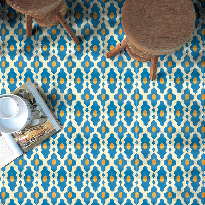 Cabana Zafini Mustard Azure 20x20cm Moroccan-style porcelain tiles shown in a styled setting with wooden stools and a magazine, featuring a repeating geometric pattern in rich blue and mustard yellow on a soft cream background with a matt finish.